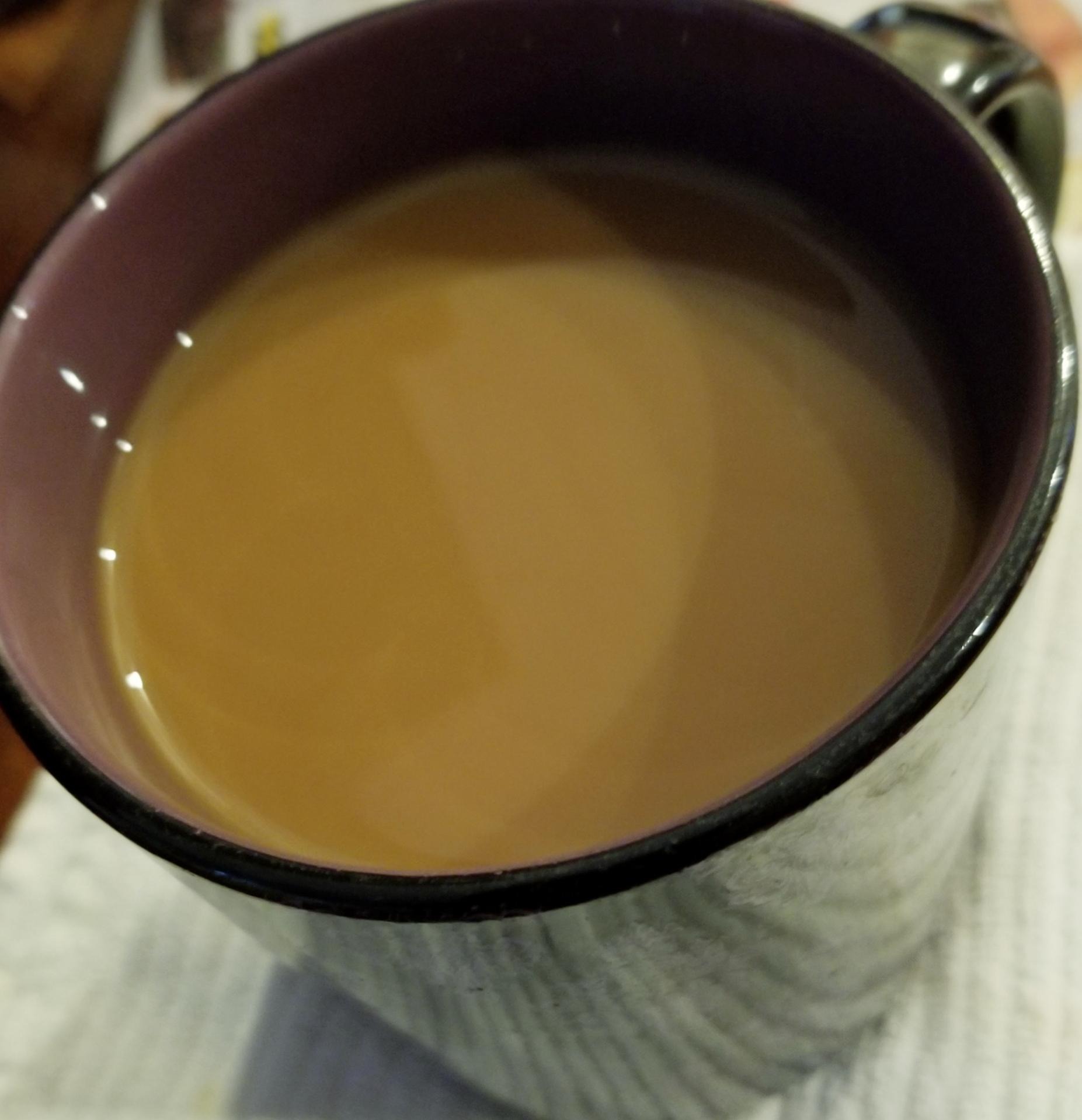 A large cup of dark coffee with milk viewed from above.