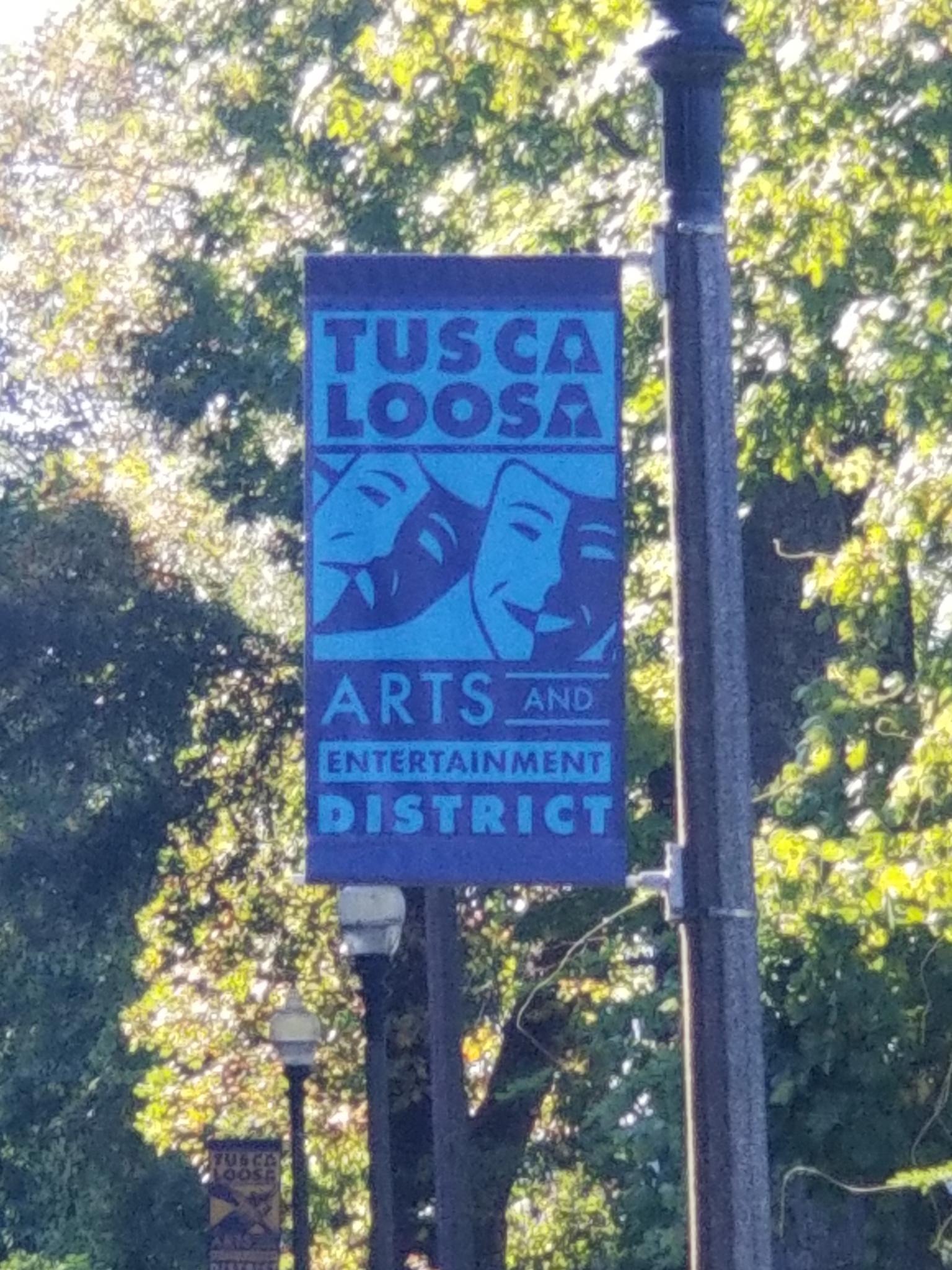 A sign marking the location of the 'Tuscaloosa Arts and Entertainment District' featuring the comedy-drama theater masks.