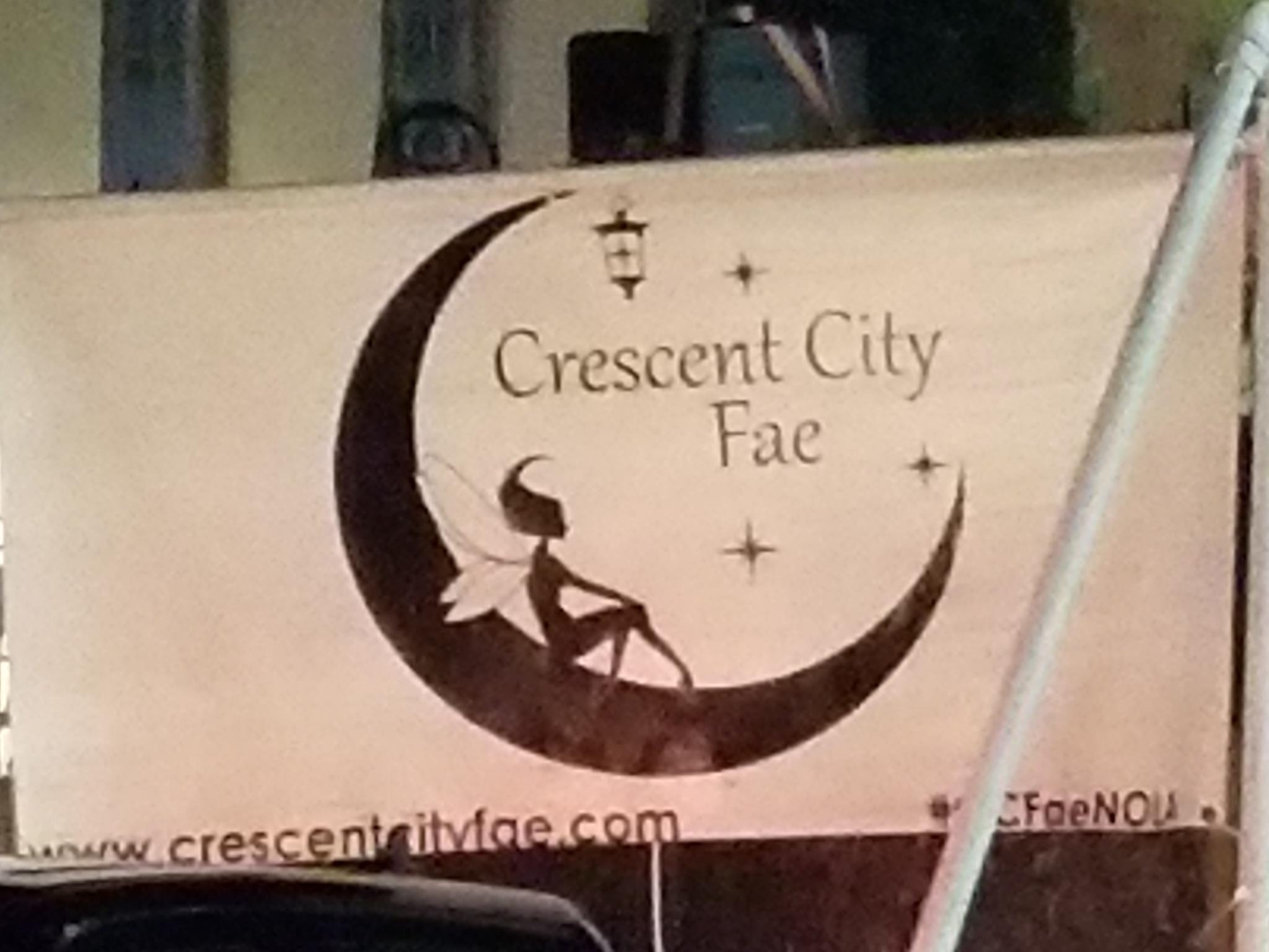 A parade banner portrays a a fairy in a crescent moon, is labeled 'Crecent City Fae' and invites the viewer to visit www.crescentcityfae.com.