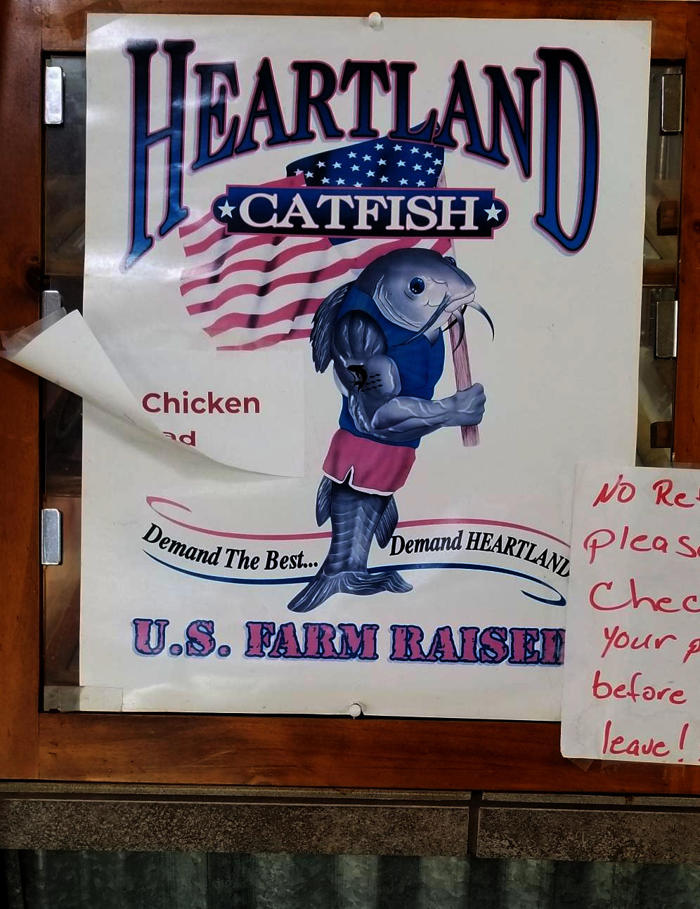 A poster located at a restaurant counter advertises Heartland Catfish, portraying a standing catfish which carries the American flag.