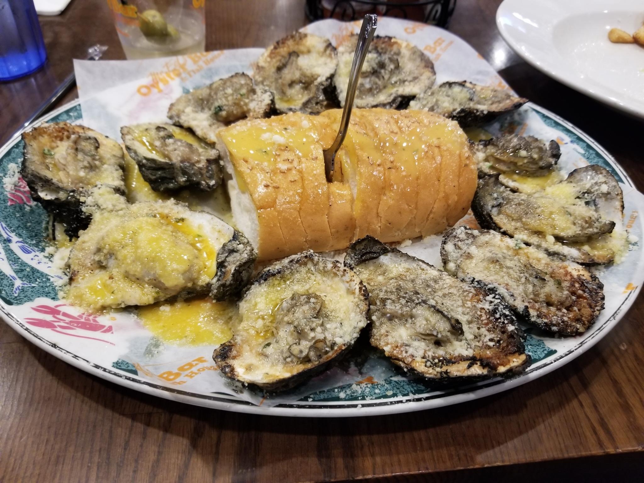 A dozen grilled oysters and french bread from which protrudes a fork.