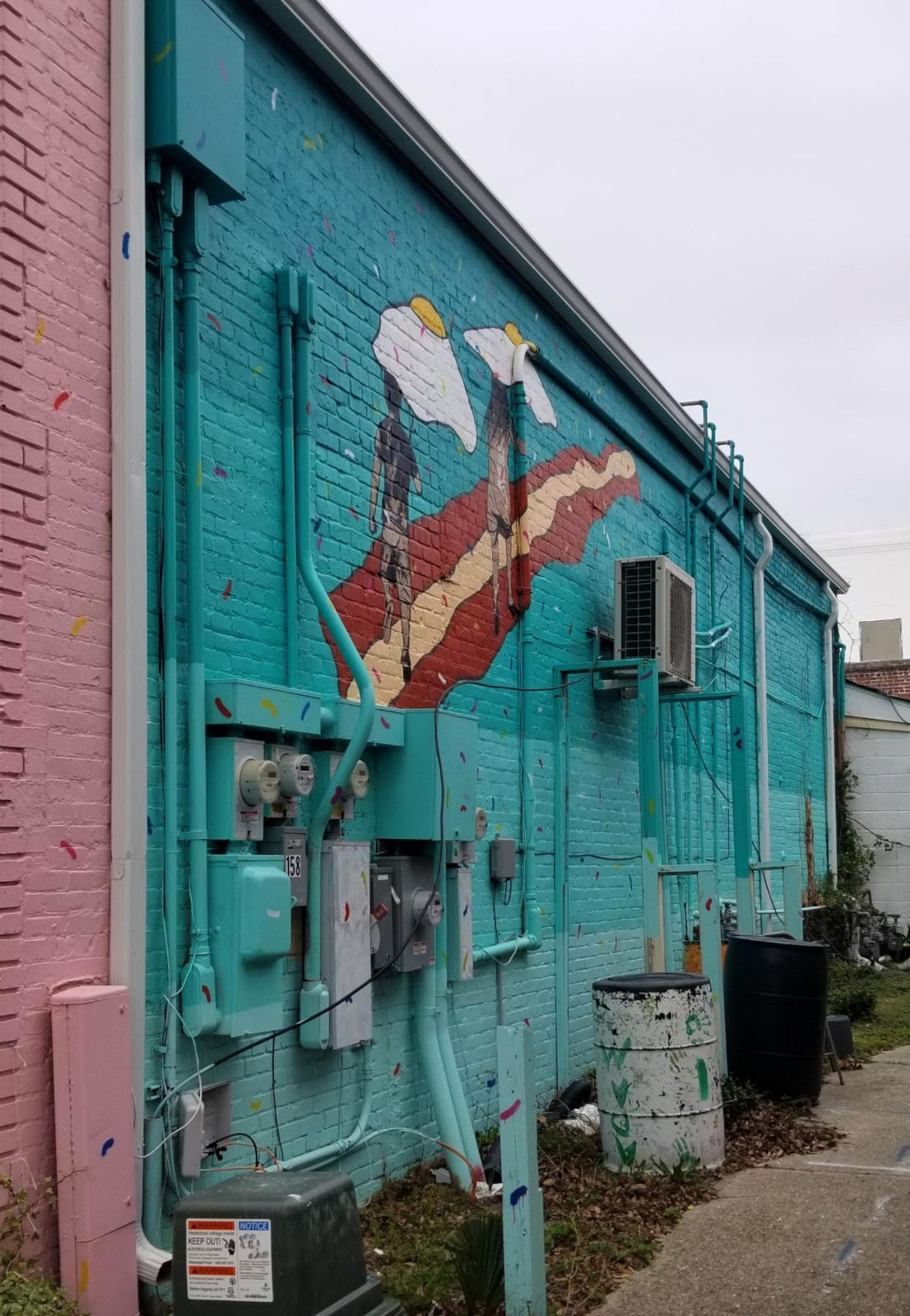 An unusual mural portrays two figures following a bacon-like road under fried-egg appearing parasols.