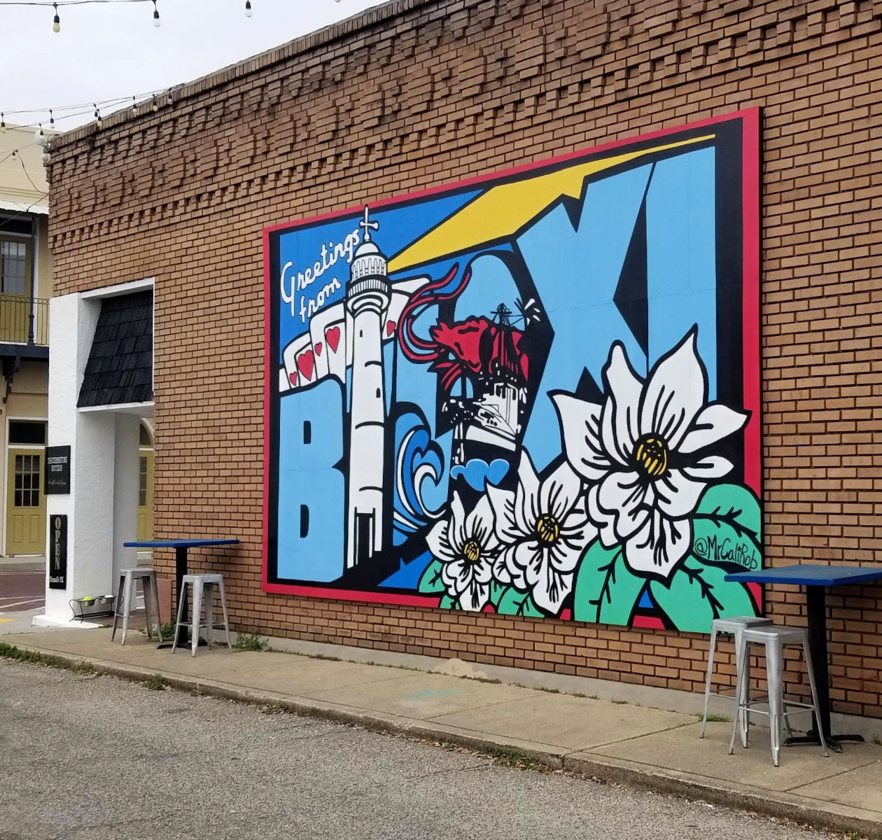 Mural portrays a message of greeting with magnolia blooms, a shrimp boat, a light house, and a hand of cards.