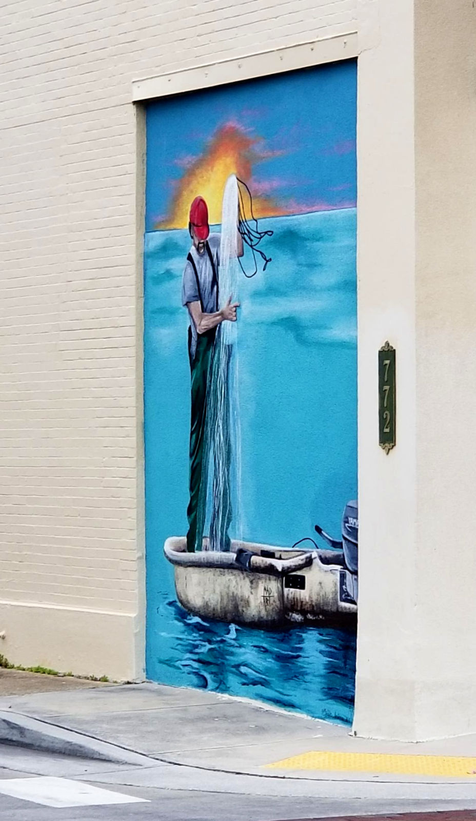Mural portrays a man pulling nets into a small boat before the setting sun.