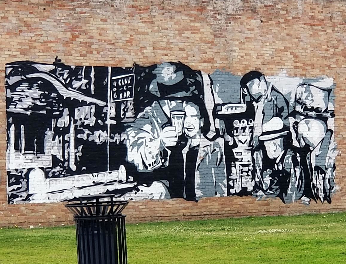 Mural on a brick wall portraying images of people gathering in a bar, in a prior era.
