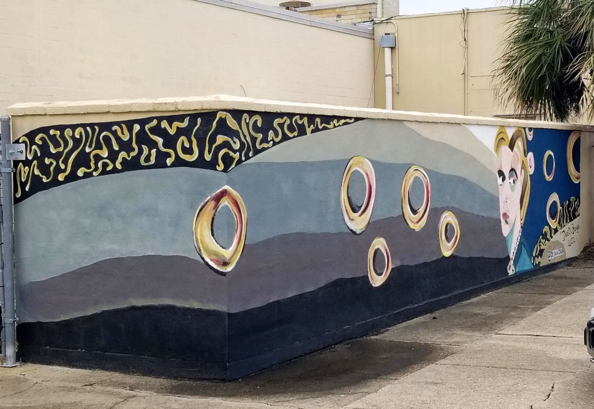 A mural seen from an alleyway includes a face that glances to the side.