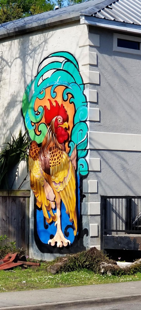 A proud-looking rooster is seen in a painting applied to the edge of a grey building.