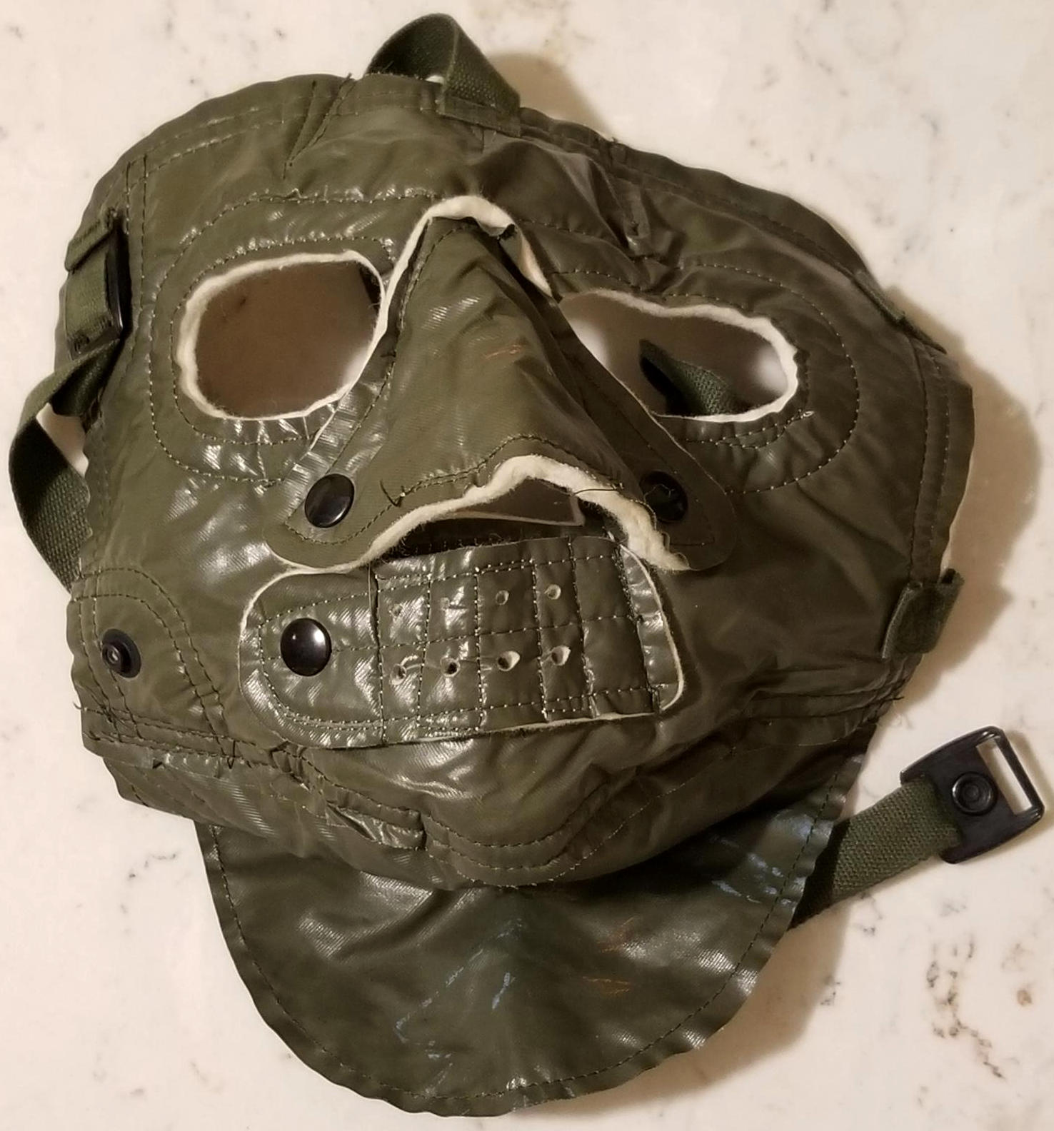 A mask intended to cover the face in extreme cold weather, the surface is green and overlays white wool. Nose and mouth coverings are secured by snaps and when fully engaged, only the eyes and nostrils are exposed.