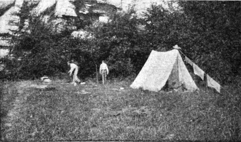 Two figures are seen at a campsite with one tent in a wooded area.
