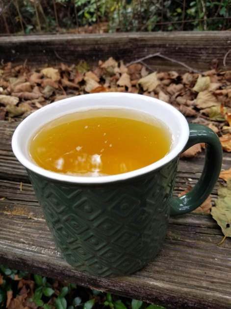 A large green cup containing turmeric-ginger tea, which is a bright golden color.