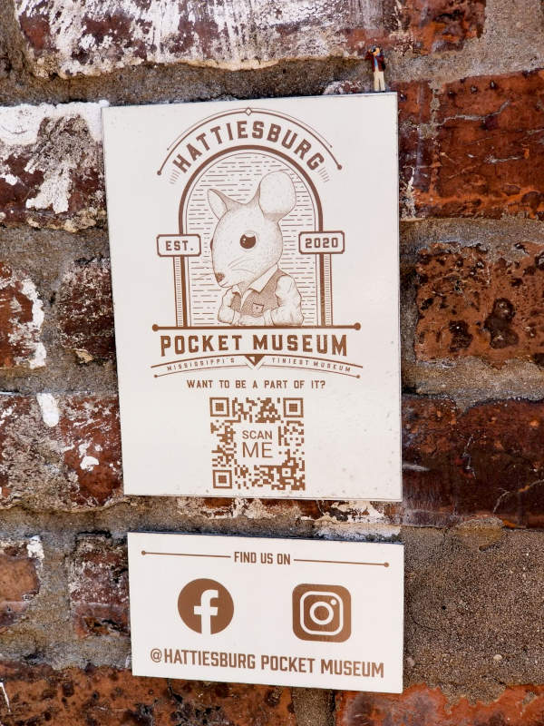 Sign on a brick wall, 'Hattiesburg Pocket Museum, Mississippi's Tiniest Museum,' and a mouse wearing a vest.