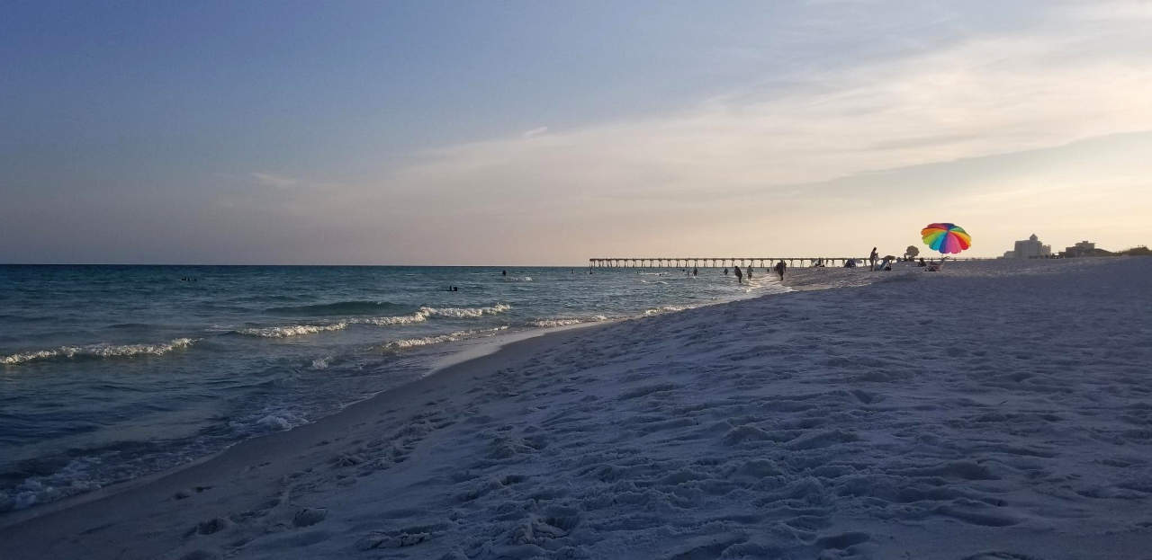 View along the beach, an umbrella visible in the distance.