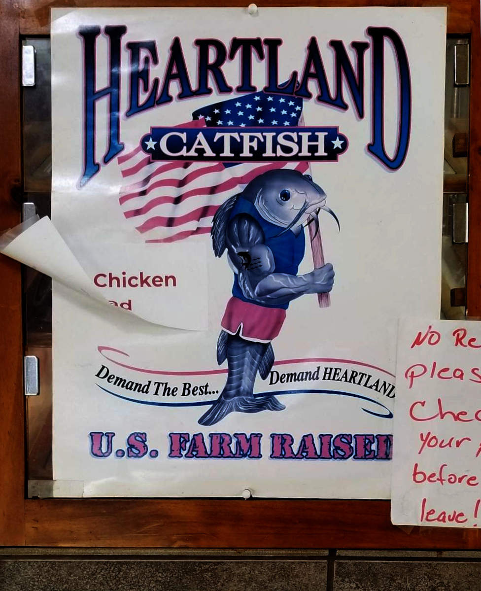 Afiŝo en restoracio reklamas Heartland Catfish, montras starantan katfiŝon kiu portas usonan flagon.