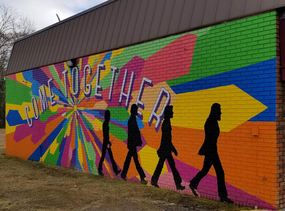 Murpentraĵo sur konstruaĵo, radiantaj koloroj, Venu Kune, kvar ombraj marŝantaj homoj kiel 'Abbey Road'.