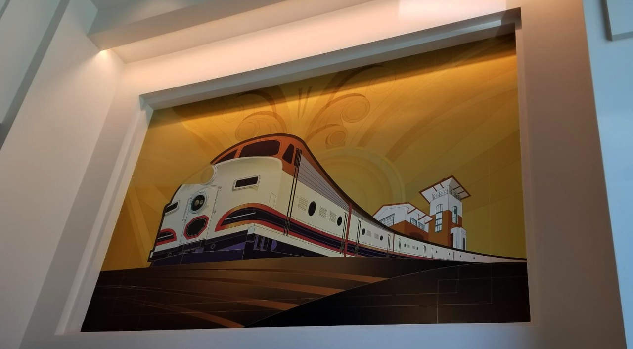 A painting shows an outgoing train leaving a modern railway station. The color scheme is coffee brown and the style is art deco.