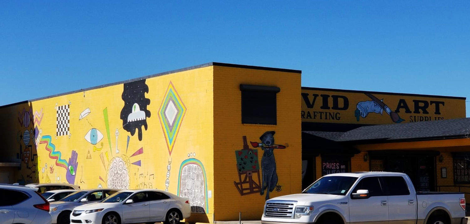 Arta Centro David www.davidartcenter.com, mustardkolora, kun multaj desegnoj, inkluzive de hundo portanta bereton, tenanta penikon antaŭ bildstablo.