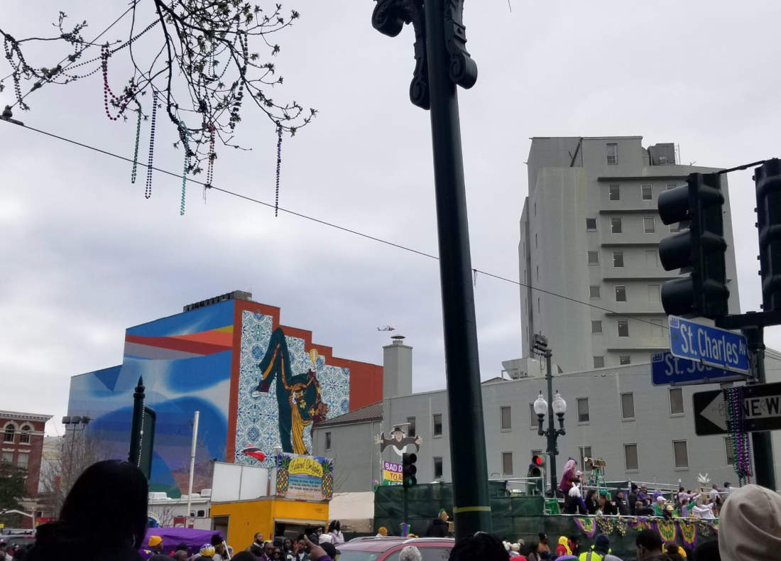 Two murals and spectators as seen from the corner of St. Charles and St. Joseph in New Orleans.