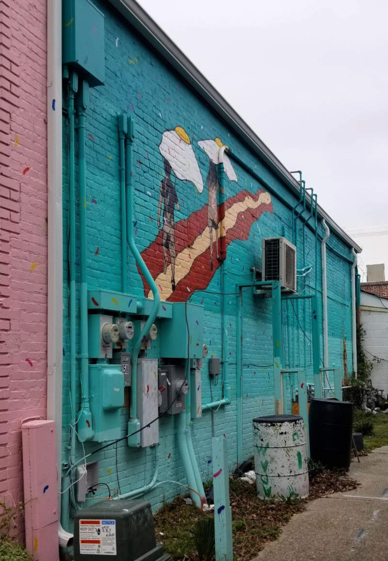 Murpentraĵo montras du homojn promenantajn sur vojo el lardo sub ombreloj de frititaj ovoj.