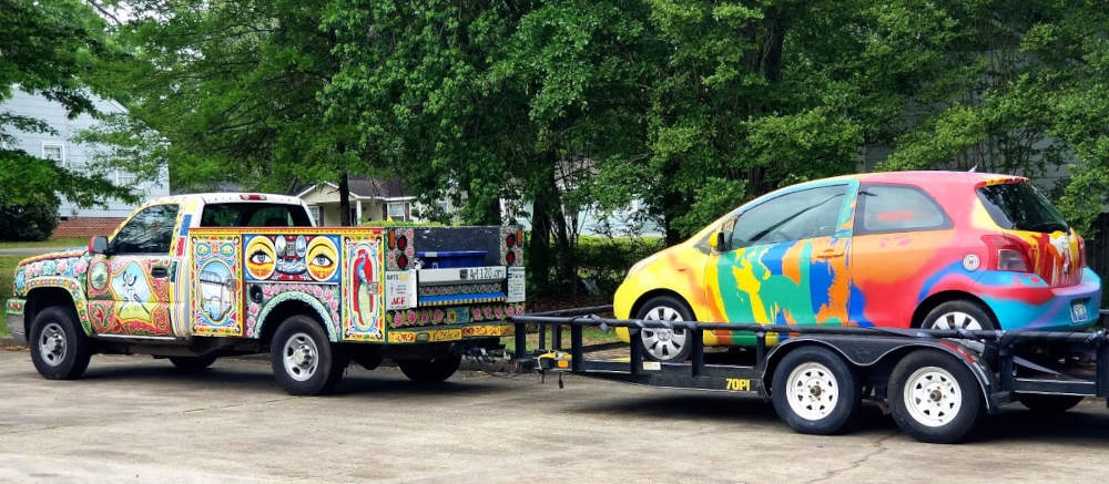 Kamiono kaj aŭto, kovritaj per artaĵo, pentritaj, buntaj.