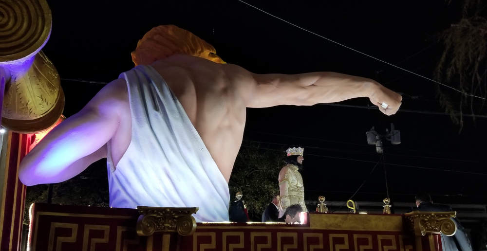 Parade float, a huge arm streches over a man who wears a crown.