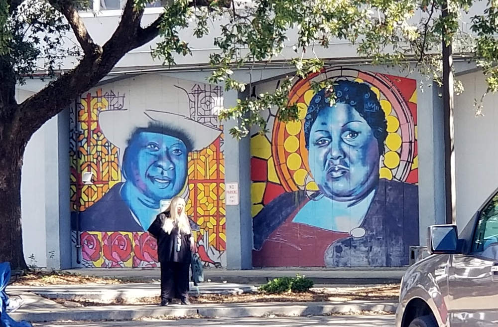 Du vizaĝoj, kun blua nuanco, en apartaj paneloj, kvazaŭ antaŭ vitralo.