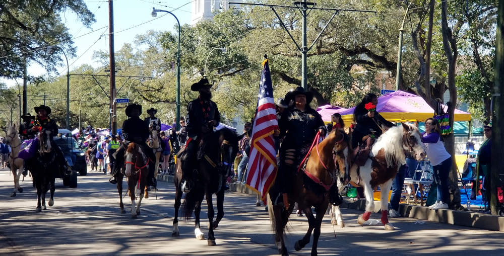 Horse-riding paraders whose leader carries the American flag.