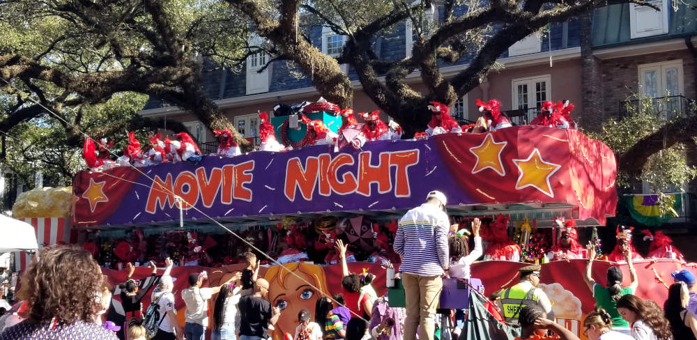 A red and purple parade float with yellow stars undeer the branches of an oak.