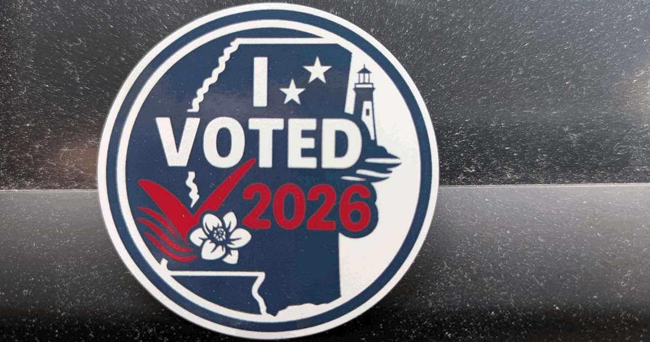 Round adhesive sticker; red, white and blue; that says "I VOTED 2026" showing the outline of Mississippi, a checkmark, a magnolia blossom, and a lighthouse.