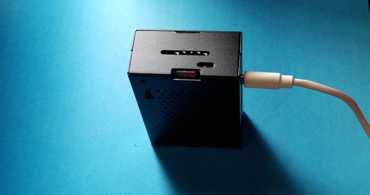 Raspberry Pi5 in an iRasptek case, plugged into USB-C, SanDisk memory card visible, indicator light shows it is operating.