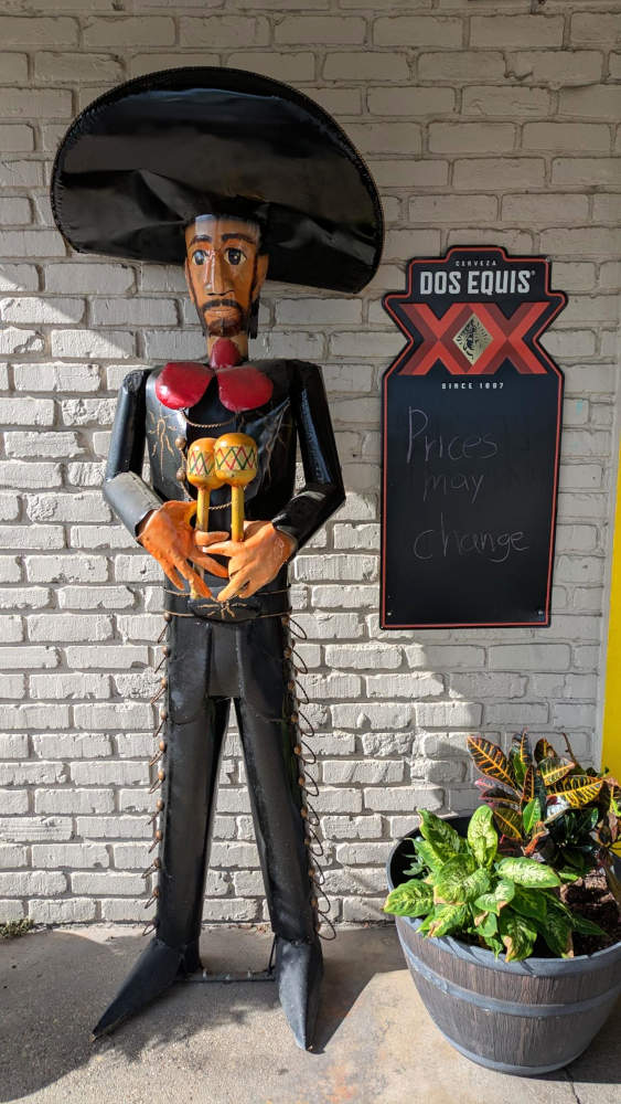 Statue of mariachi holding maracas, sign says 'Prices may change.'