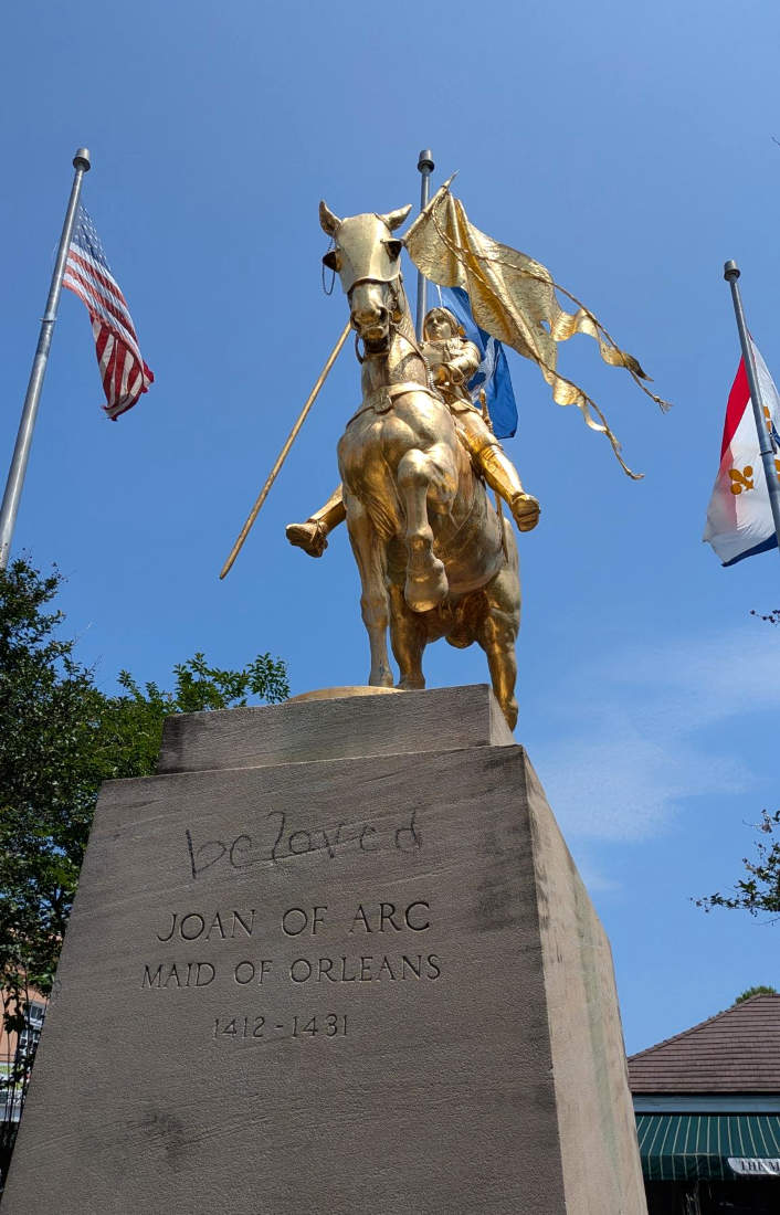 Statuo, fraŭlino sur ĉevalo, kirasita, portanta flagon, tute ora, sur piedestalo, grafitiita per 'amata', gravurita per 'Joan d'Arc, Fraŭlino de Orleano, 1412-1431'