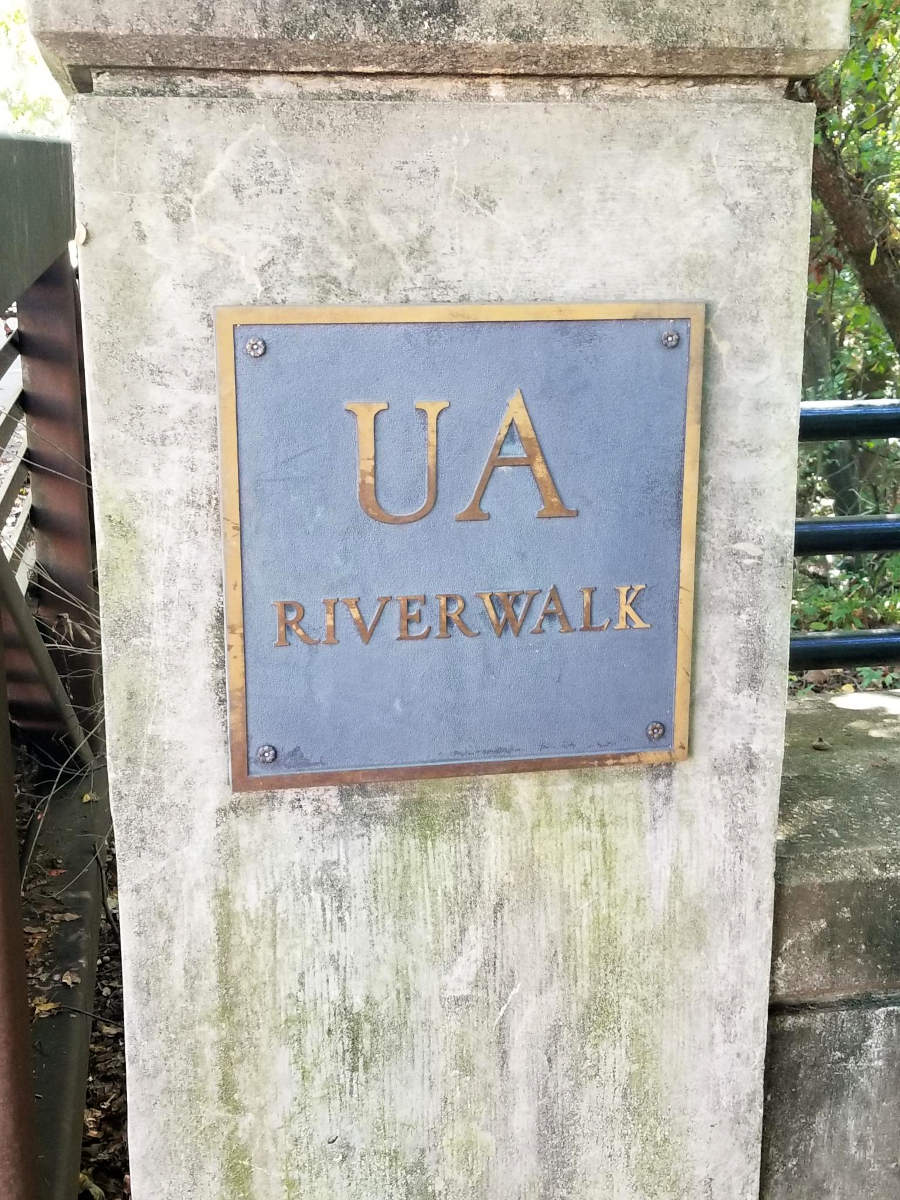 A brass sign on a pillar marks the UA Riverwalk.