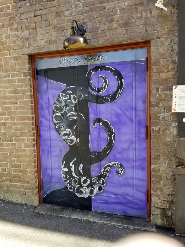 Purple exterior doors, 'Free Hugs', and it looks as if one door is open and a giant octopus is extending its tentacles from beyond.
