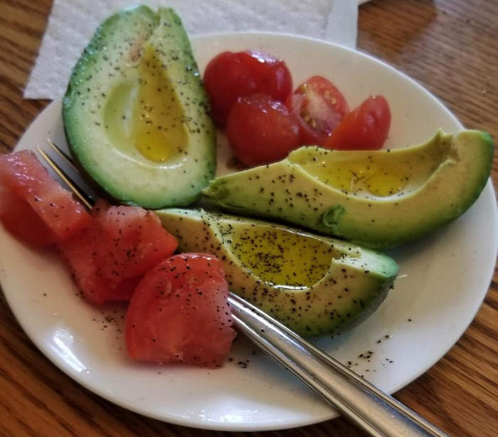 A salad of avocado and tomato with olive oil and black pepper.