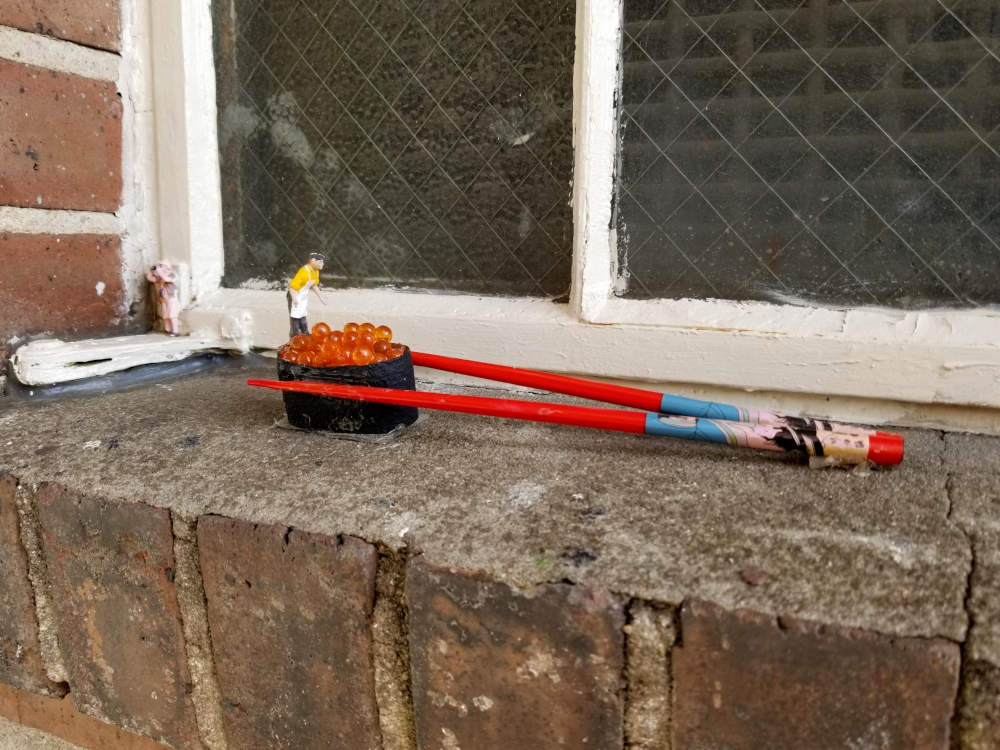 Sculpture on a windowsill, a little man bends over sushi with chopsticks.