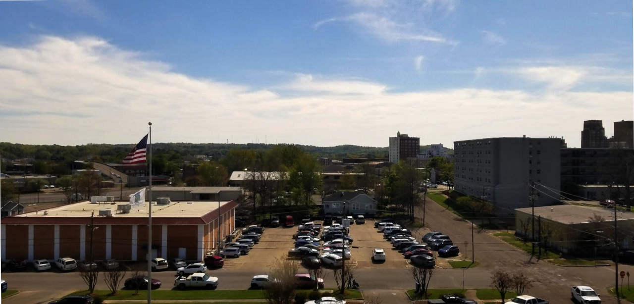 Buildings, partking lot,  cars, hills beyond.