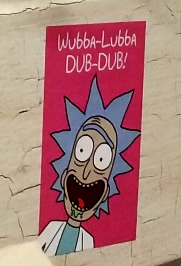 A sticker on a wall shows a drawn face from 'Rick and Morty', Wuba-Luba Dub-Dub.