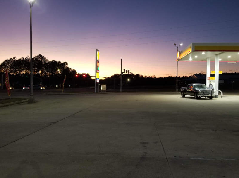 A sunset seen in the distance from a gas station parking lot.