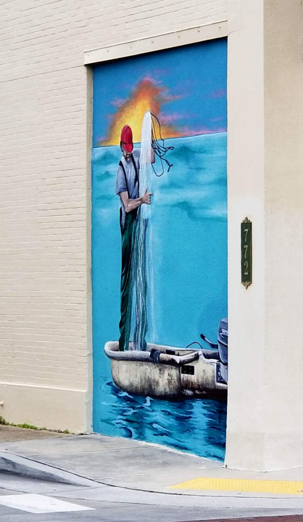 Mural, a man pulling nets into a small boat before the setting sun.
